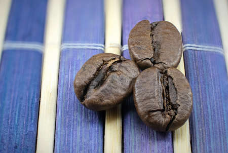 Macro of three coffee beans on purple and white wooden trivet