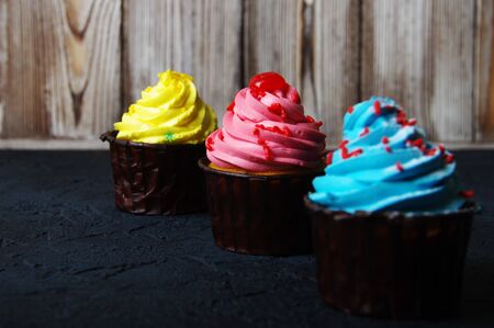 Cupcake cakes yellow, pink, blue on a dark background