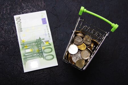 Shopping cart full of coins and Euro banknotes on dark backgroundの写真素材