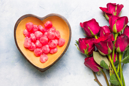 Many heart shaped candy Packed in a heart-shaped wooden cup With a bouquet of roses Placed on blue-white surface.の写真素材