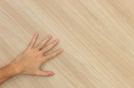 The man's left hand carries a gold ring on his finger on a wooden floor.の写真素材