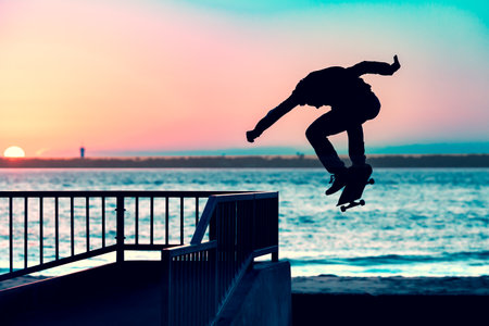 Unrecognizable teenage boy silhouette showing high jump tricks on scooter against orange sunsetwarm...