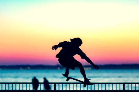 Unrecognizable teenage boy silhouette showing high jump tricks on scooter against orange sunsetwarm...