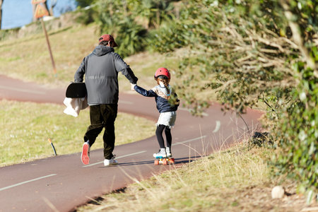 father teaching his daughter skateboarding on a bike pathの写真素材