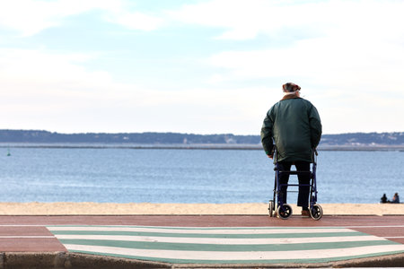 Elderly man sitting on walker looking out over beachの写真素材