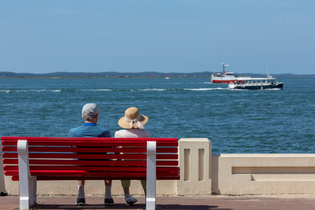 Rear view of an older couple sitting close together on a bench looking out over the water.の写真素材