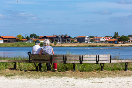 Rear view of an older couple sitting close together on a binch looking out over the water.の写真素材
