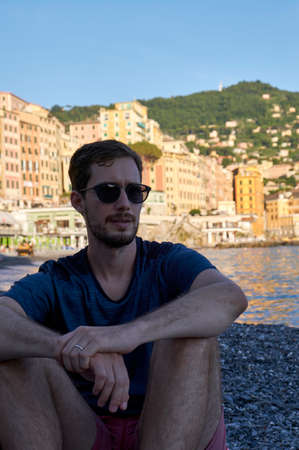 a portrait of a young model men wearing sunglasses on the beach of Camogli, Genova, Italy, with the colorful houses behindの写真素材