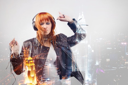 Beautiful smiling red-haired girl in  leather jacket, with flowing hair, enjoying music in...