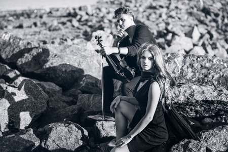 violinist and the girl sitting on stones on sea shoreの写真素材