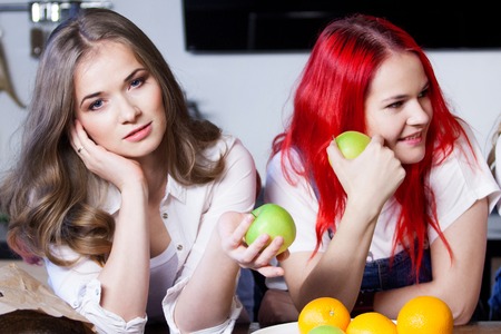 two young girls in the kitchen talking and eating fruit