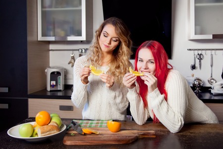 two young girls in the kitchen talking and eating fruitの写真素材