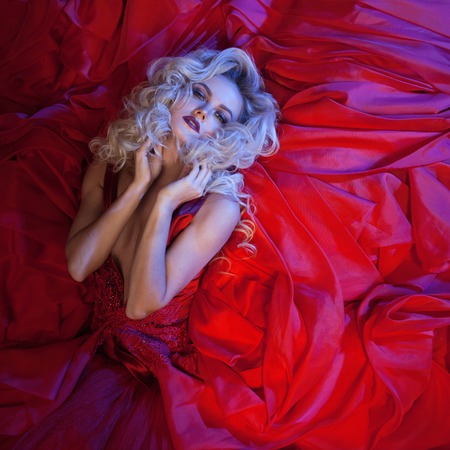 Fashion photo of young magnificent woman in red dress. Studio portrait. Seductive blonde in dress with fluffy skirtの写真素材