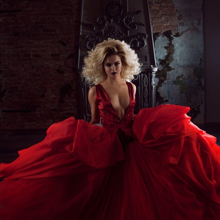 Fashion photo of young magnificent woman in red dress. Running towards camera. Seductive blonde in dress with fluffy skirtの写真素材