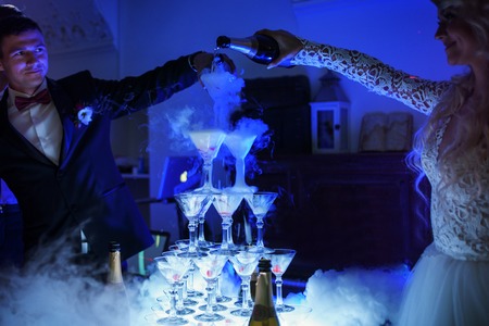 married couple are pouring champagne into the pyramid of glasses