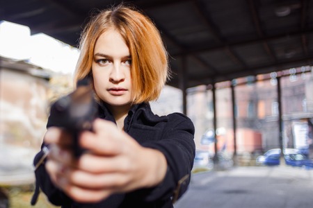 Woman pointing a gun. Girl shooting at someone on the street.の写真素材