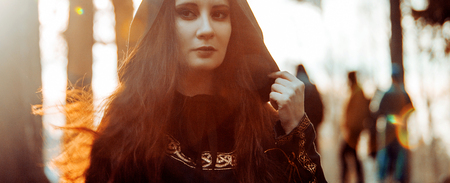 Young beautiful and mysterious woman in the woods, in a black cloak with a hood, the image of a...
