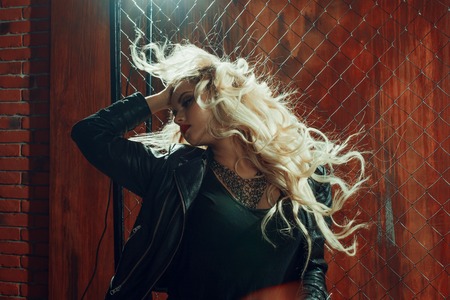 Rock'n'roll girl, young beautiful girl dances in a dark alley, against the fence meshの写真素材