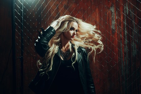 Rock'n'roll girl, young beautiful girl dances in a dark alley, against the fence meshの写真素材
