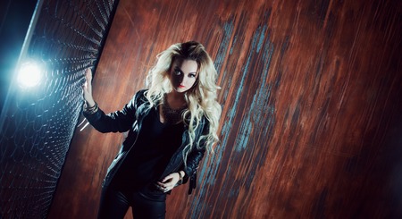 Rock'n'roll girl, young beautiful girl dances in a dark alley, against the fence meshの写真素材