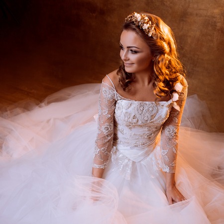 Beautiful girl bride in a luxurious wedding dress, portrait in Golden tones, the effects of glareの写真素材