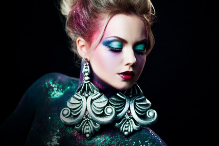Young attractive blonde girl in a bright art-makeup, high hair, body painting. Rhinestones and...