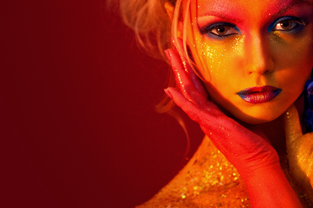 Portrait of young and attractive woman with art makeup. Fiery colors, glitter on face and floral decorationの写真素材