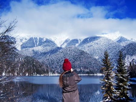 Traveler in the mountains, girl in jacket and hat stands on shore of mountain lake. Mountain gorge, beautiful Northern landscapeの写真素材