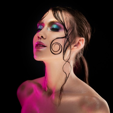 Young beautiful girl bright makeup with a wet look shine, dark backgroundの写真素材