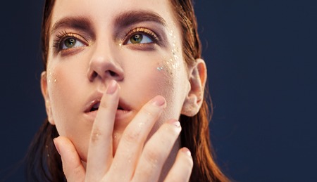 Close up portrait of beautiful woman with creative gold make up. touching lips