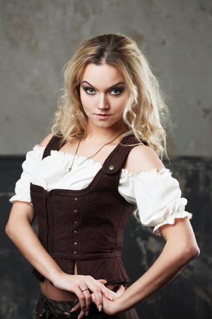 Portrait of a beautiful steampunk woman in a pant suit with vest, over grunge background.の写真素材