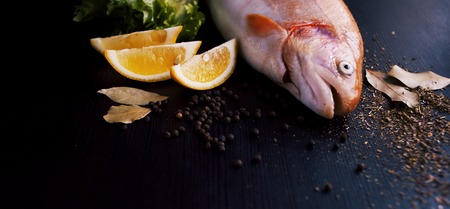 Fresh trout and ingredients to prepare fish dishes on black tableの写真素材