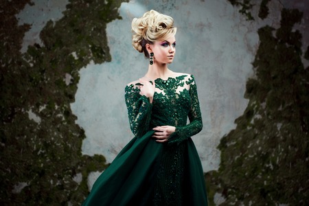 Portrait of young attractive blonde woman in a beautiful green dress. Textured background, interior. Luxury hairstyleの写真素材