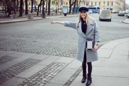 Young, hip and attractive blonde hailing taxi , girl in a stylish hat and a gray coatの写真素材