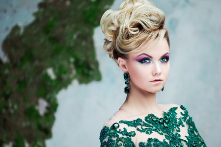 Portrait of young attractive blonde woman in a beautiful green dress. Textured background, interior. Luxury hairstyleの写真素材
