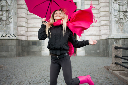 Beautiful young and happy blond woman with colorful umbrella on the street. The concept of positivity and optimismの写真素材