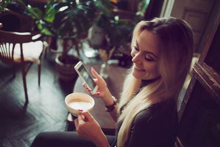 Young female freelancer chatting on mobile phone while sitting on the couch in vintage cafeの写真素材