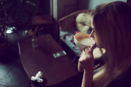 Young charming female freelancer chatting on mobile phone while sitting on the couch in vintage cafe. Drink morning coffee in comfortable coffee shopの写真素材