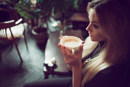 Young charming female freelancer chatting on mobile phone while sitting on the couch in vintage cafe. Drink morning coffee in comfortable coffee shopの写真素材