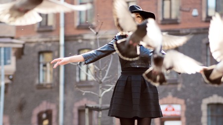 Young girl in a stylish hat, in the street playing with a large number of pigeons. Birds fly upの写真素材