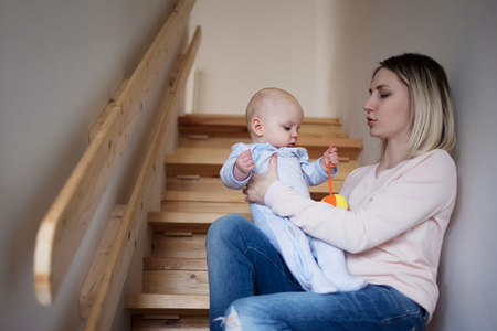 Young mother with a child sitting on the stairs, house.の写真素材