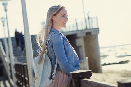 Young cheerful girl on the seashore. Young blonde walk on the promenade. Trendy beige skirt