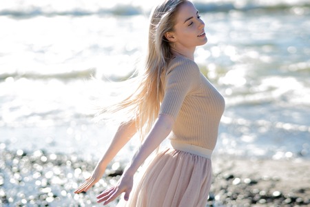Young cheerful girl on the seashore. Young blonde woman smiling. Open arms hugs the oceanの写真素材