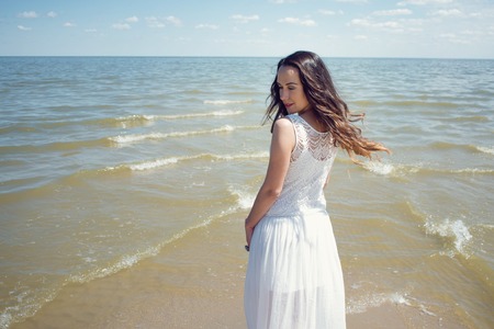 Young beautiful brunette woman in white dress on the seashore. Back viewの写真素材