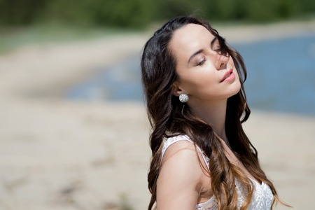 Young beautiful brunette woman in white dress on the seashore. portrait with closed eyesの写真素材