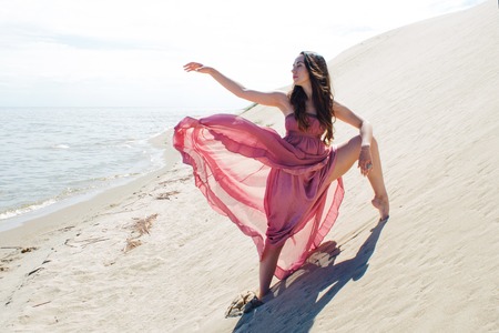 Woman in red waving dress with flying fabric runs on background of dunes. Gymnast on the back of the duneの写真素材