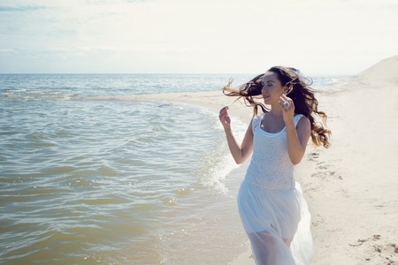 Young beautiful brunette woman in white dress on the seashoreの写真素材
