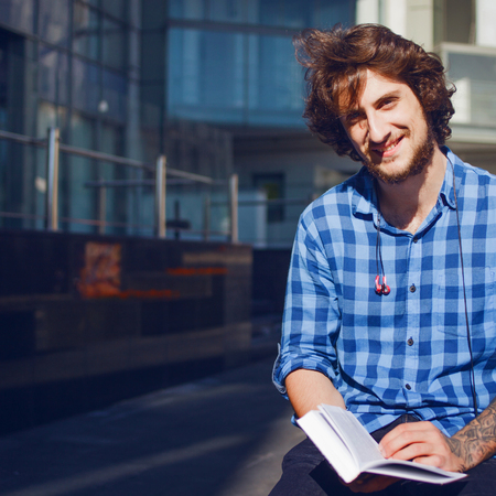 Guy in the blue shirt reading a book and smiling. Portrait of young handsome stylish man on the street.の写真素材