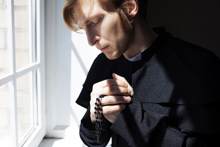 Portrait of handsome young catholic priest praying to God.
