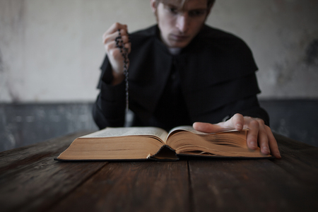 Page of Bible, close-up. Portrait of handsome young catholic priest. Focus on the handの写真素材